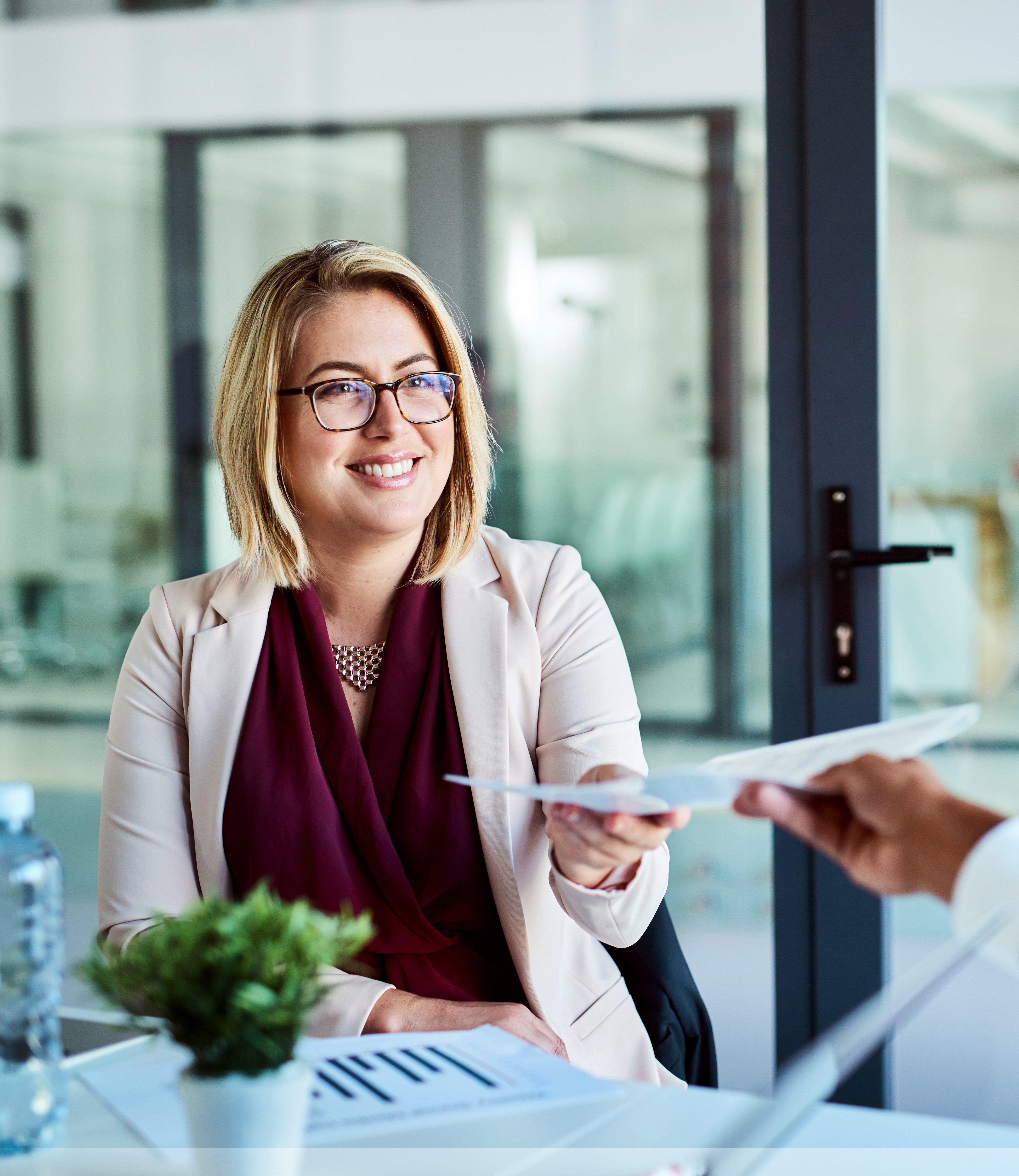 woman seated at desk being handed a document
